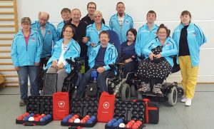Boccia_1000x600 Gruppe von Sportlern in Sportjacken mit Boccia-Ausrüstung in der Halle.