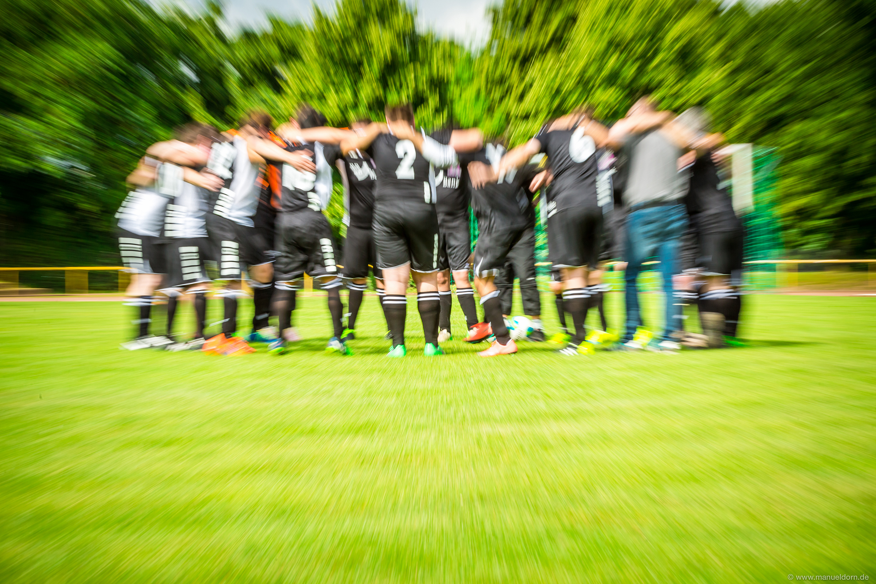 Mannschaft in Schwarz bei einer Besprechung auf dem Fußballfeld.