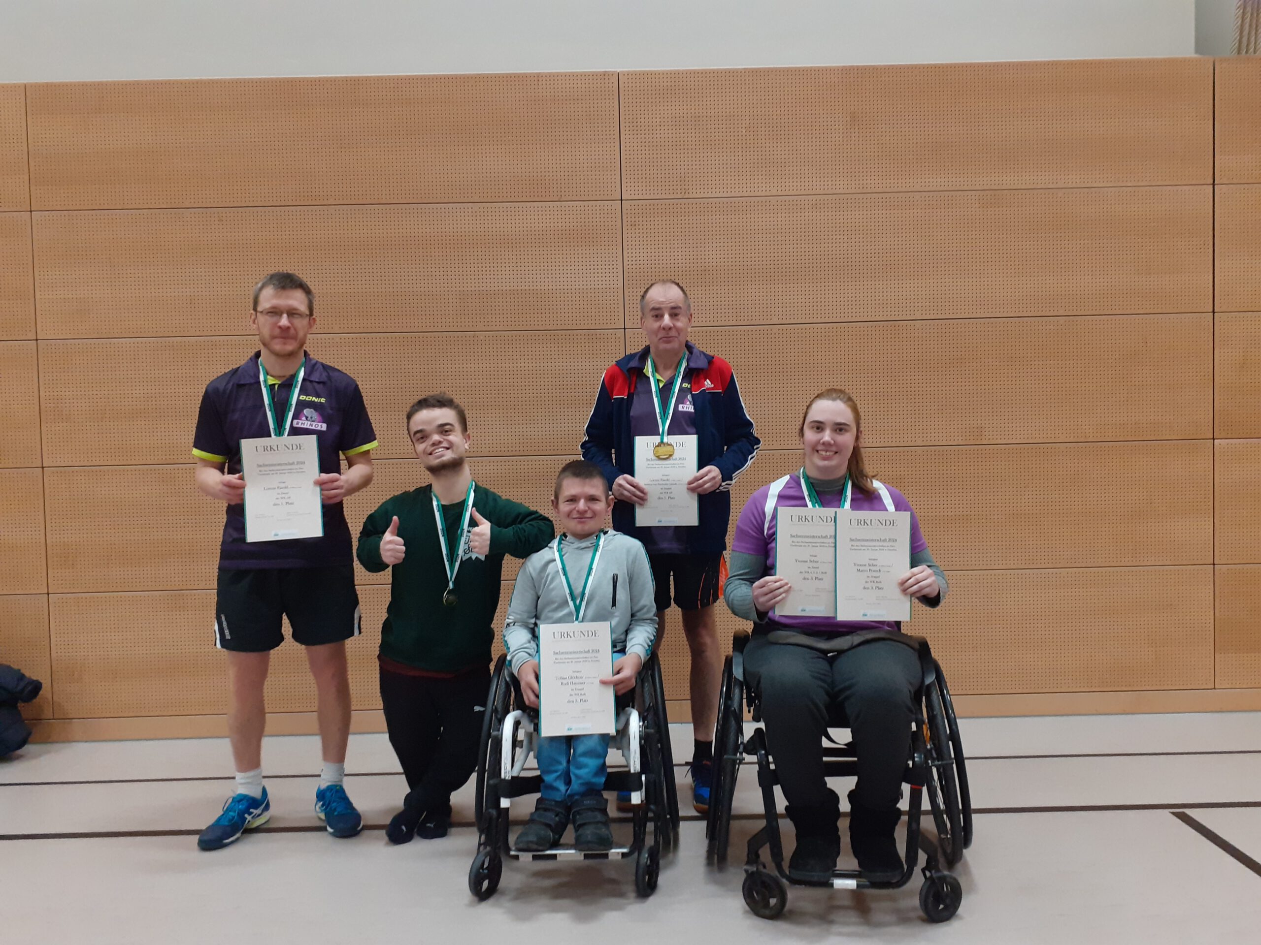 Fünf Sportler mit Urkunden und Medaillen in einer Sporthalle.