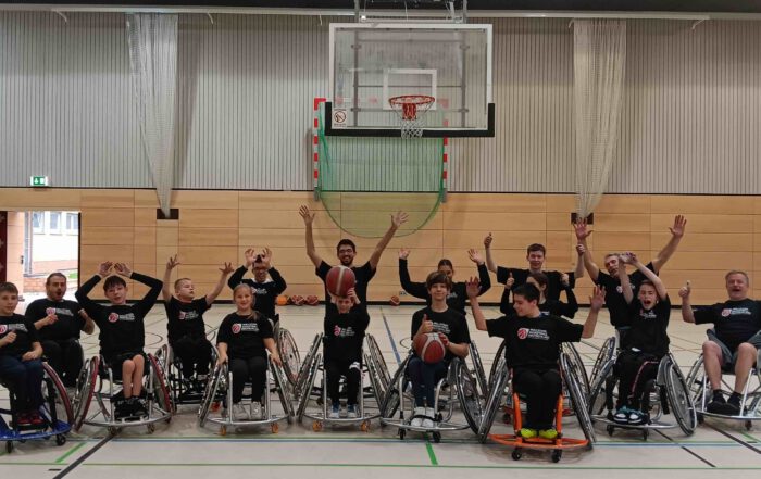 Gruppe von Rollstuhlbasketballern in der Halle, alle jubeln und halten Bälle.