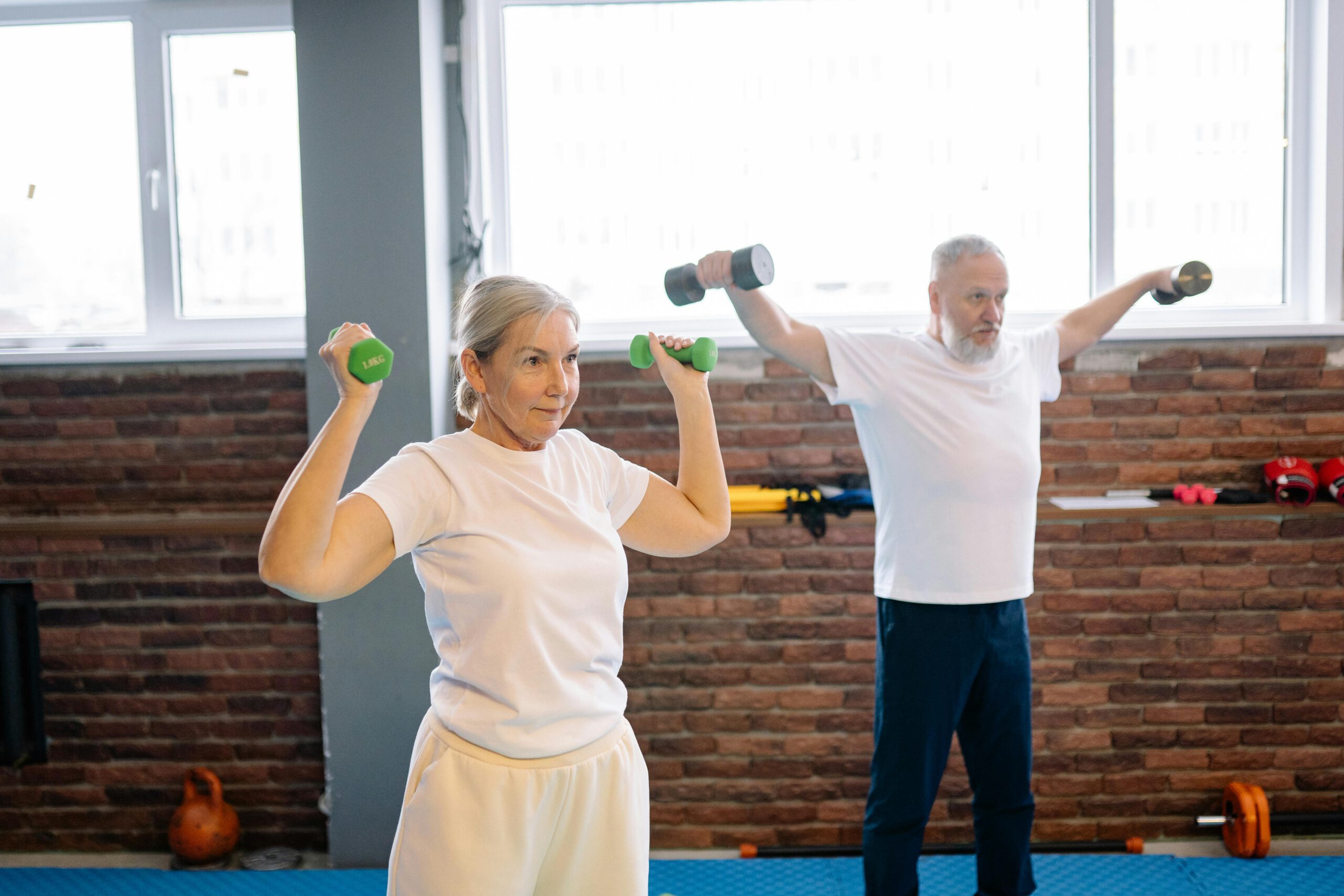 Zwei Personen beim Krafttraining mit Hanteln in einem Fitnessraum.
