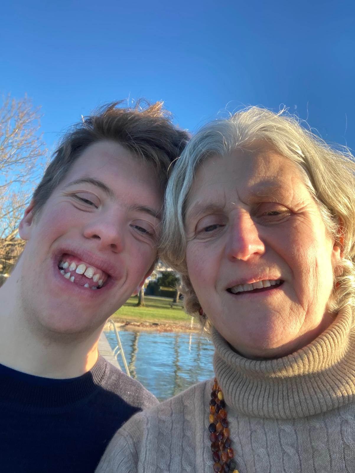 Sportbuddy Philipp und seine Mama lächeln in die Kamera, im Hintergrund ein Gewässer und Bäume.
