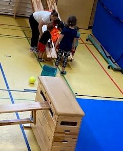 Trainerin unterstützt ein Kind im Rollstuhl beim Überqueren eines Sprungkastens – inklusives Training bei den Rhinos Kids