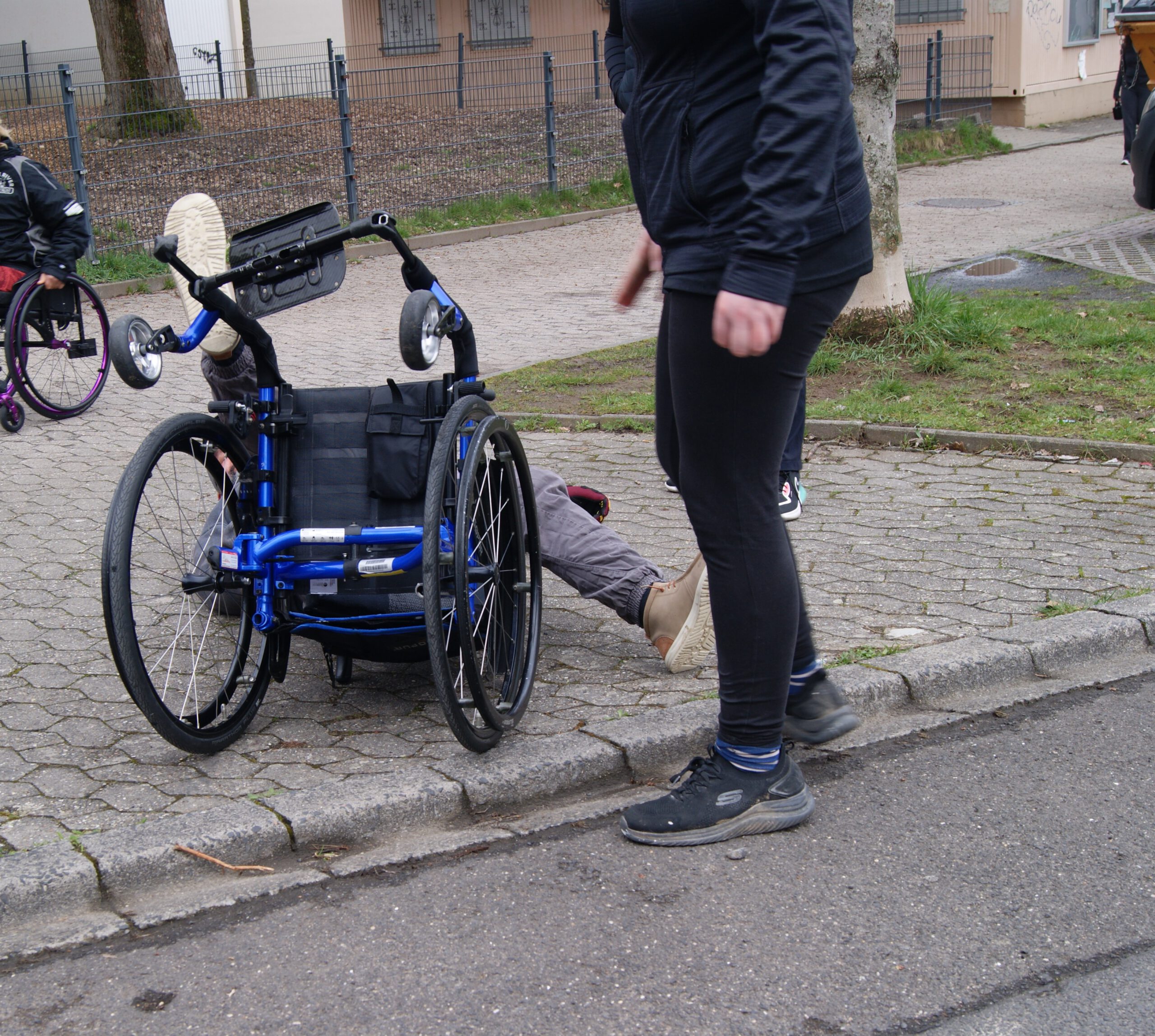 Rollifahrer liegt rücklings auf dem Biden, neben ihm ein Trainer, sie übern das aufstehen, nachdem man umgefallen ist