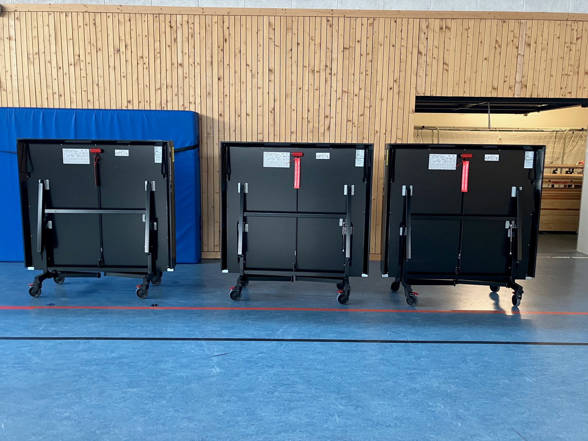Drei zusammengeklappte, barrierefreie Tischtennistische auf Rollen, aufgereiht in der Trainingshalle des SV Rhinos Leipzig