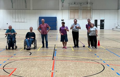 Gruppenfoto der Boccia-Mannschaft in einer Sporthalle, Spielerinnen und Spieler stehend und im Rollstuhl mit Boccia-Bällen in der Hand