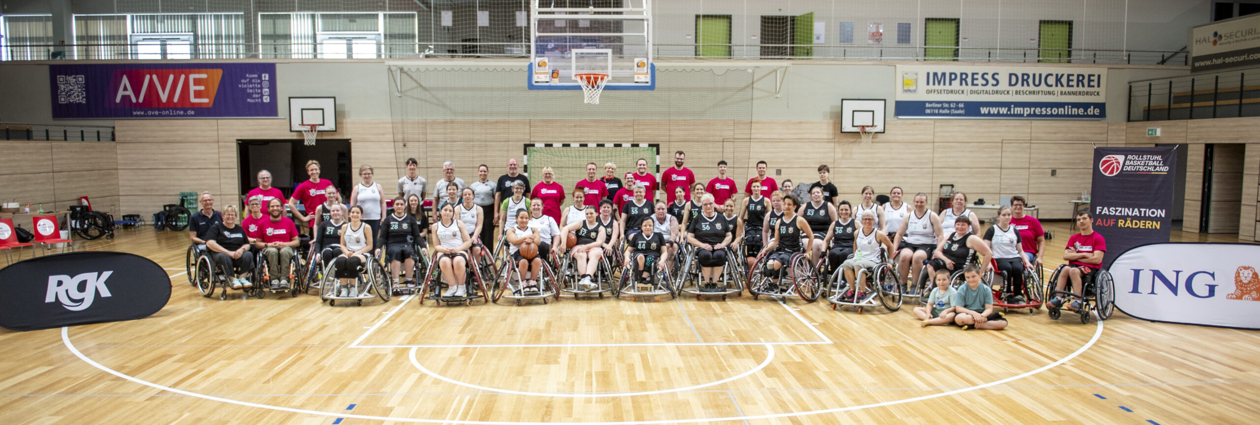 Panorama-Gruppenfoto aller Queens-Cup-Teams in Rollstühlen aufgereiht in einer Sporthalle in Halle an der Saale, mit Sponsorenbannern.
