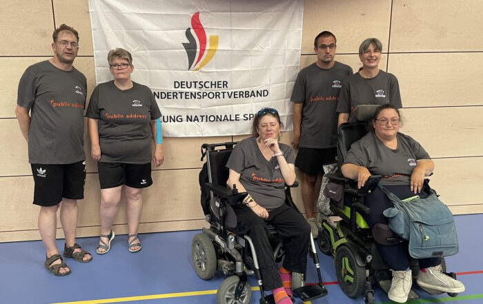 Sechs Boccia Rhinos aus Wiesbaden posieren vor einem Banner des Deutschen Behindertensportverbands in der Sporthalle in Weiden, zwei davon in Rollstühlen.