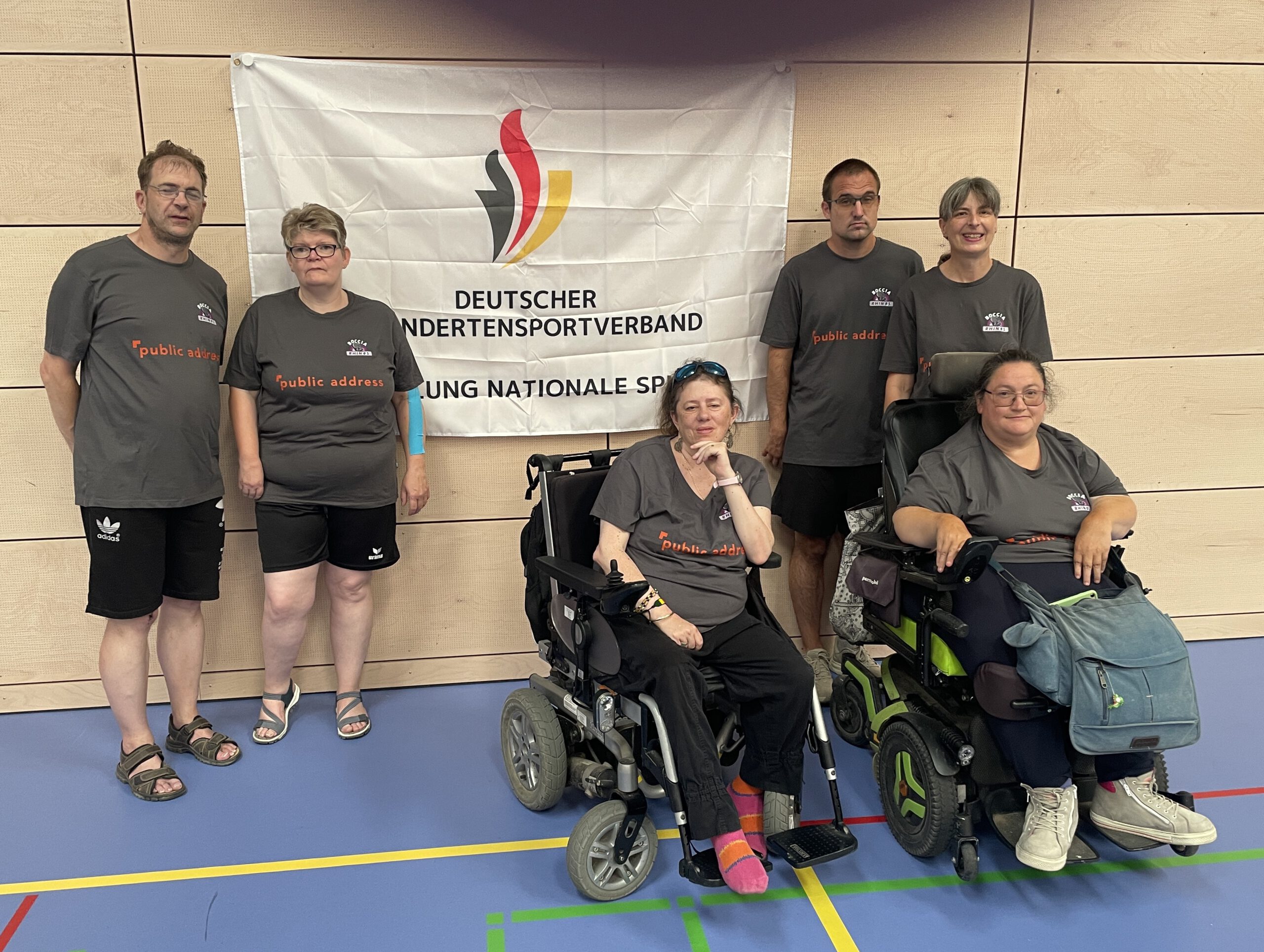 Sechs Boccia Rhinos aus Wiesbaden posieren vor einem Banner des Deutschen Behindertensportverbands in der Sporthalle in Weiden, zwei davon in Rollstühlen.