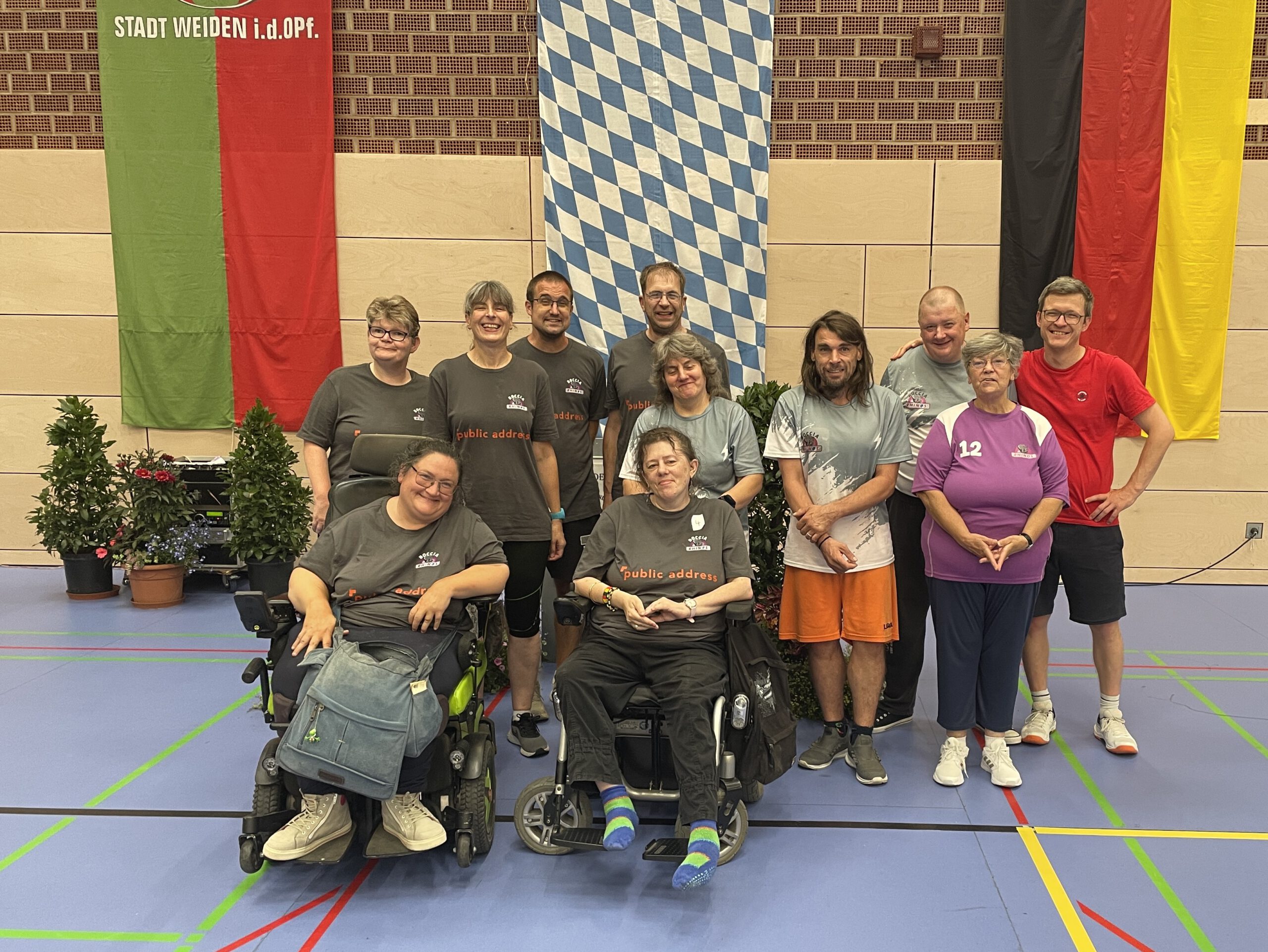 Großes Gruppenfoto mehrerer Boccia-Mannschaften nach der Deutschen Meisterschaft in Weiden, im Hintergrund Fahnen der Stadt Weiden und Bayerns.