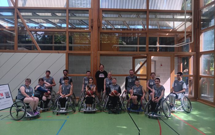 Gruppenfoto der 13-köpfigen Rhinos-Mannschaft in Wiesbadener Trikots in einer lichtdurchfluteten Sporthalle mit Glasfenstern.