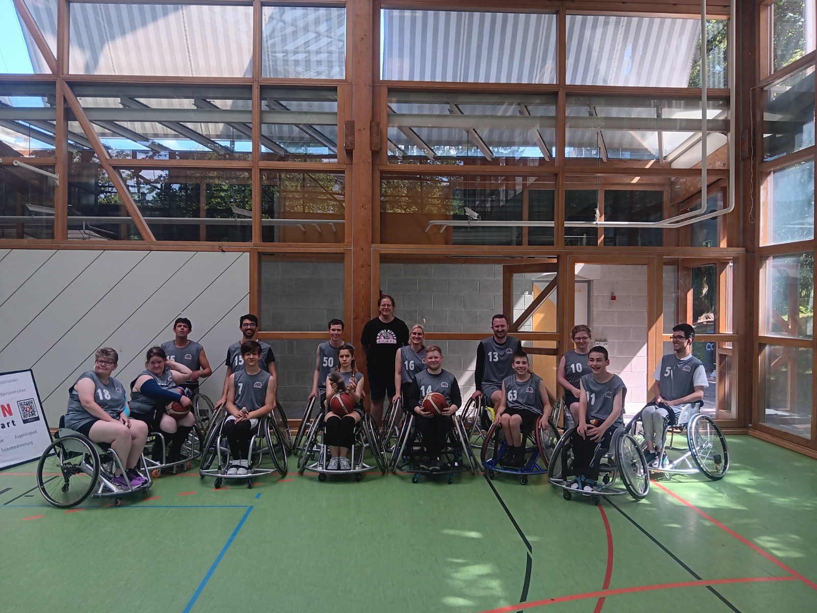 Gruppenfoto der 13-köpfigen Rhinos-Mannschaft in Wiesbadener Trikots in einer lichtdurchfluteten Sporthalle mit Glasfenstern.
