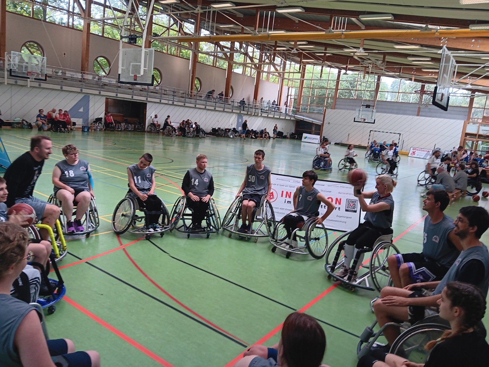 Rhinos-Spielerinnen und -Spieler mit Rollstühlen im Kreis in einer Sporthalle vor Beginn des Turniers in Stuttgart, im Hintergrund ein „Inklusion im Sport